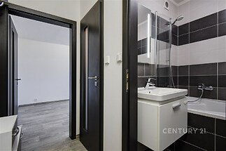 Koupelna s moderními dlaždicemi, sprchou a vanou. Vedlejší dveře vedou do předsíně s laminátovou podlahou. Světlý a praktický interiér.