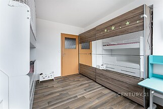 Dětský pokoj s dřevěnou podlahou, vestavěné skříně a moderní palanda, světlý prostor ideální pro rodinu.