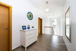 Chodba s dlažbou, světlá stěna, moderní osvětlení a dřevěné dveře. Velké zrcadlo opticky zvětšuje prostor v moderní novostavbě.