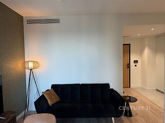 Světlý obývací pokoj s parketovou podlahou, moderní sedačkou a stylovým osvětlením, vedoucí do prostorné chodby s dlažbou.