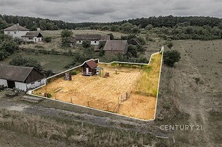 Stavební pozemek s rovinatým terénem, obklopený zelení, vhodný pro výstavbu rodinného domu, s přístupem po zpevněné cestě.