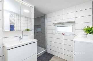Moderní koupelna s dlažbou, sprchovým koutem a vestavěnou umyvadlovou skříňkou, poskytující praktický a stylový prostor pro každodenní použití.