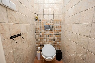 Toaleta s dlažbou, světle hnědé mozaikové obklady, moderní nádržka, kompaktní prostor, vhodné pro rekonstrukci.