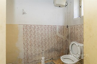 Prázdné WC s oprýskanými stěnami, dlažba a malým oknem, určené k rekonstrukci, vhodné pro modernizaci a individuální úpravy