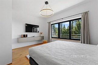 Světlá ložnice s parketovou podlahou, velkými okny a moderním osvětlením, poskytující krásný výhled do přírody.