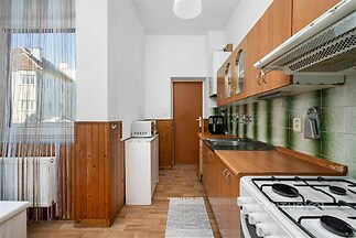 Kuchyň s dřevěnými skříňkami, parketovou podlahou a velkým oknem, nabízí světlý interiér s plynovým sporákem a moderním vybavením.