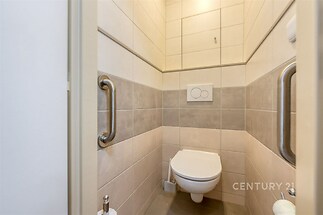 Samostatná toaleta s moderní dlažbou, nerezová madla pro pohodlí, čistý a světlý interiér, zánovní keramika a splachovací systém.