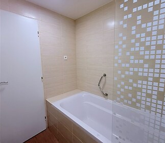 Moderní koupelna s dlažbou a vanou, světlé obklady doplněné skleněnou zástěnou, čisté linie a jednoduchý design, připravená k okamžitému užívání.