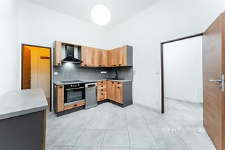 Moderní kuchyň s dlažbou, světlým dřevem a vestavěnými spotřebiči, prostorná a světlá s moderními prvky, ideální pro pohodlné bydlení.