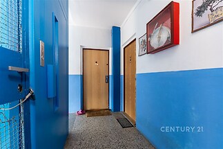 Vstupní hala s dlažbou, dvěma dřevěnými dveřmi a starším výtahem, ideální pro bytový dům.