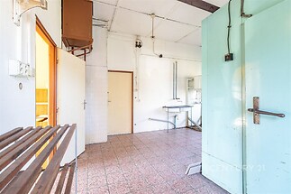 Prádelna s dlažbou, světlá stěna, původní stav, plynový kotel, dřevěný regál, vysoký strop, dveře na toaletu, vhodné pro rekonstrukci