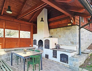 Krytá zahradní terasa s kamenným grilem a moderní kuchyňskou linkou, dlážděná podlaha, dřevěné obložení, ideální pro venkovní posezení