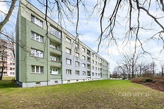 Bytový dům s moderní fasádou a velkými okny, obklopený zeleným trávníkem, ve světlém prostředí blízkosti přírody.