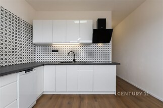 Moderní kuchyň, bílá lesklá dvířka, parketová podlaha, elegantní dlažba, světlý prostor.