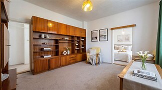 Světlý obývací pokoj s dřevěným nábytkem, vestavěné skříně, moderní styl, koberec na podlaze, dobře osvícený prostor.