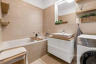 Moderní koupelna s keramickými obklady, prostornou vanou a vestavěnou skříňkou. Světlé tóny a moderní vybavení dodávají prostoru elegantní vzhled.