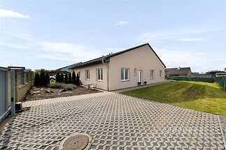 Bungalov s prostornou dlážděnou terasou, moderní fasádou a upravenou zahradou, nabízí klidné bydlení v rezidenční čtvrti.