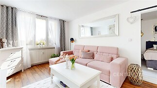 Světlý obývací pokoj s parketovou podlahou, velká okna a moderní design. Přirozené osvětlení a stylové dekorace vytvářejí útulnou atmosféru.