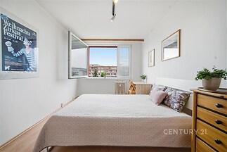 Světlá ložnice s parketovou podlahou, velkými okny a moderním nábytkem, poskytuje útulné a příjemné prostředí.