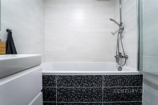 Kachlová koupelna s moderní vanou, sprchovou baterií a světlými obklady, vytvářející elegantní a čistý design.