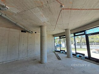 Světlý komerční prostor s betonovými stěnami, velkými okny a moderními konstrukčními prvky, ideální pro podnikání v atraktivní lokalitě.