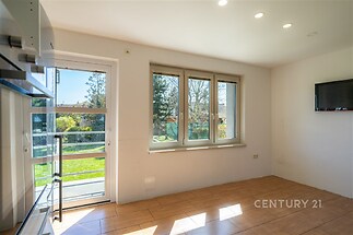 Světlá kuchyň s dlažbou, velkými okny a moderním osvětlením, výhled do zahrady, ideální pro rodinné bydlení.