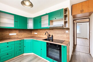 Moderní kuchyň s dřevěnými povrchy a zelenými skříňkami, vestavěná trouba, laminátová podlaha, světlá a otevřená dispozice.