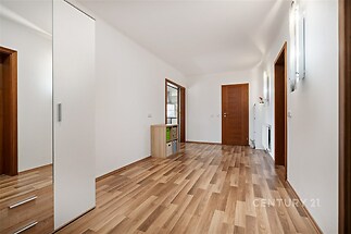 Prostorná předsíň s parketovou podlahou, světlým moderním nábytkem a dřevěnými dveřmi nabízí praktické vestavěné skříně pro úložný prostor.