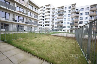 Uzavřený dvůr s trávníkem a dlažbou, obklopený moderními bytovými domy s balkony, ideální pro rezidenční bydlení v novostavbě.