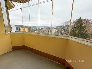 Prosklený balkon s výhledem na město, betonová podlaha, dřevěné obložení, vhodný k rekonstrukci, možnost úprav podle potřeb.