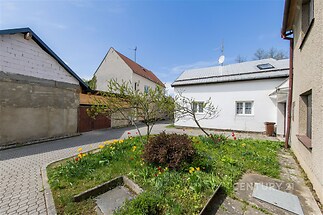 Dvorek s květinovou zahradou, dlážděná cesta a tradiční omítkou pokryté domy, klidná lokalita.