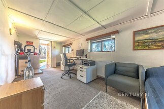 Domácí kancelář s kobercovou podlahou, světlá místnost s okny na zahradu, moderně zařízené s pracovním stolem a pohodlným křeslem.