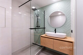 Moderní koupelna s proskleným sprchovým koutem, dřevěným umyvadlovým pultem a světlými obklady, které dodávají prostoru elegantní vzhled.