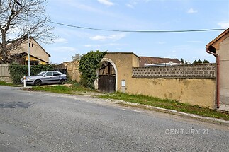 Venkovní prostor s kamennou zdí, vjezdová brána, vedlejší stavba, venkovský styl, klidná lokalita.