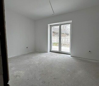 Prázdná místnost s betonovou podlahou, velkými okny a bílými stěnami, připravena pro rekonstrukci nebo úpravy podle moderních standardů.