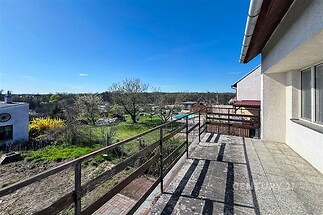 Prostorná terasa s dlažbou a dřevěným zábradlím nabízí panoramatický výhled do okolní zeleně, ideální pro relaxaci na čerstvém vzduchu.