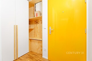 Vstupní chodba s parketovou podlahou, vestavěné skříně s dřevěným dekorem a jasně žluté dveře, moderní a svěží design.