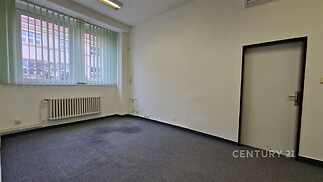 Prázdná kancelářská místnost s kobercovou podlahou, velkými okny a bílými stěnami, ideální pro komerční využití.
