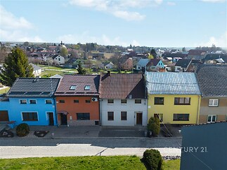 Řadové rodinné domy v malebné vesnici, s barevnými fasádami a plechovými střechami, na klidné dlážděné ulici, ideální pro rodinné bydlení.