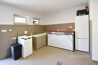 Praktická prádelna s dlažbou, velkým mrazákem a pračkou. K dispozici také prostorný dřez a úložný prostor, ideální pro běžnou údržbu domácnosti.