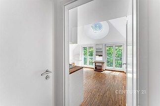 Světlý obývací pokoj s parketovou podlahou, velkými okny a moderním designem, který nabízí ideální prostor pro útulné bydlení.