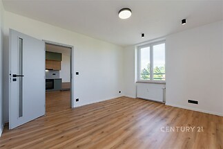 Světlý obývací pokoj s parketovou podlahou, velká okna poskytují dostatek přirozeného světla, moderní design v rekonstruovaném bytě.