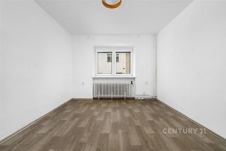 Prázdný pokoj s parketovou podlahou, bílými stěnami a velkým oknem, které zajišťuje dostatek světla, ideální pro moderní úpravy.