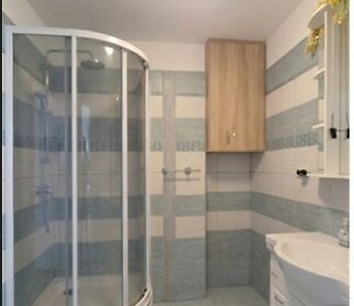 Koupelna s moderní sprchovým koutem, dlažba ve světlých odstínech, vestavěná skříňka, světlý interiér.