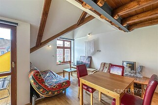 Podkrovní obývací pokoj s dřevěnými trámy, moderním nábytkem a velkými okny, které poskytují dostatek přirozeného světla.