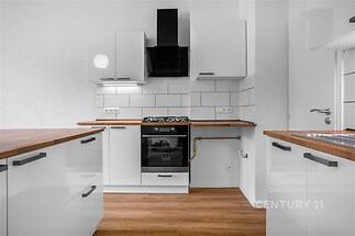 Moderní kuchyň s lesklými skříňkami, parketovou podlahou a dřevěnou pracovní deskou, stylová digestoř a vestavěná trouba.