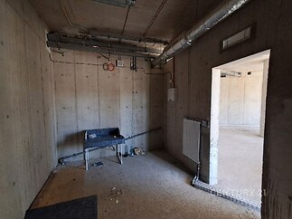 Nezařízená místnost s betonovými stěnami, industriální styl, kovové potrubí, hrubá povrchová úprava.