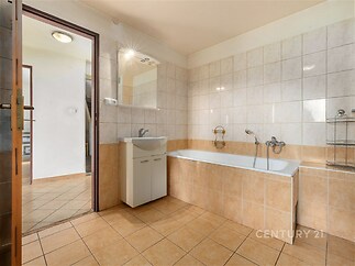 Koupelna s dlažbou, moderní vanou a světlými obklady. Prostorná a dobře osvětlená, perfektně udržovaná pro pohodlí.
