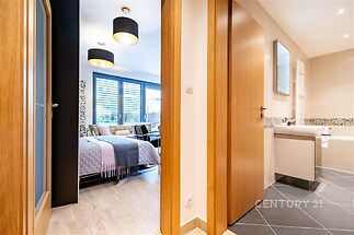 Moderní ložnice s dřevěnou podlahou a velkými okny vedle rekonstruované koupelny s dlažbou, světlé prostory pro komfortní bydlení.