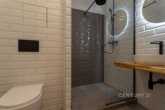 Moderní koupelna se sprchovým koutem, obložení s bílými dlaždicemi a skleněnou příčkou, elegantní umyvadlo na dřevěné desce, stylový design.